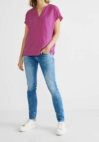 Rosa kortärmad topp med vita prickar, V-ringning, i kombination med ljusblå skinny jeans och vita sneakers. Slät textur, avslappnad passform.