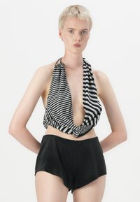 Gestreepte haltertop in zwart en wit met een diepe V-hals en knoopdetail, gecombineerd met hoge zwarte corduroy shorts.