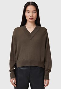 Maglione a V in verde oliva, realizzato in morbido materiale a maglia; presenta spalle cadenti e polsini a costine, abbinato a pantaloni in pelle nera.