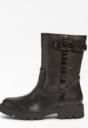 Bottine en cuir noir avec une semelle épaisse, détail de boucle sur le côté et accents de sangle texturés. Fini lisse avec un bout rond.