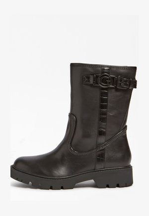 Botín de cuero negro con suela gruesa, detalle de hebilla lateral y acentos de correa texturizada. Acabado suave con punta redonda.