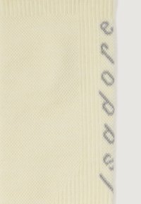 Țesătură tricotată texturată crem, cu margine în dungi și text vertical parțial în litere gri.