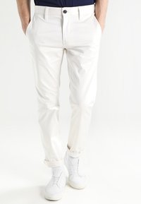 Vita bomullshängselbyxor med rak passform, med sidofickor och en enskild knäppning. Uppvikta fållar visar en mjuk textur.