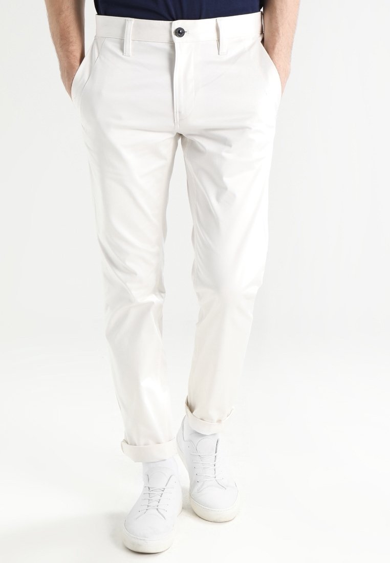 Vita bomullshängselbyxor med rak passform, med sidofickor och en enskild knäppning. Uppvikta fållar visar en mjuk textur.