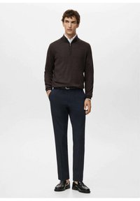 Brązowy sweter na zamek, granatowe spodnie i czarne buty. Sweter ma fakturowaną powierzchnię; spodnie są dopasowane; buty wykonane z gładkiej skóry.