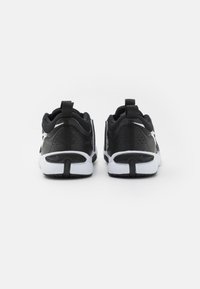 Baskets de sport noires avec un design texturé, dotées d'une semelle blanche et d'accents au talon. Comprend des languettes au talon pour un enfilage facile.