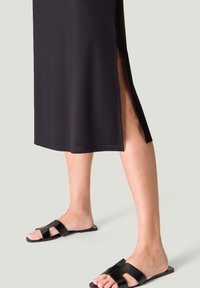 Musta midi-mekko, jossa on sivuhalkiot, valmistettu sileästä kankaasta. Yhdistetty mustiin liukumekkoihin, joissa on kaksoishihnadesign.