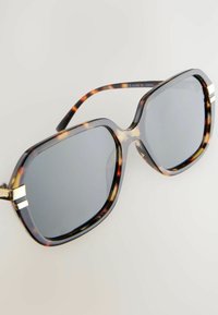 Überdimensionale Sonnenbrille mit einem Schildpatt-Rahmen, grauen Gläsern und goldenen Akzentstreifen an den Schläfen, die eine glänzende Oberfläche aufweisen.