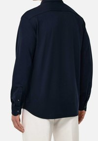 Náměsíčně modrá košile s dlouhým rukávem a manžetami na knoflíky, rovného střihu a hladké textury, s detailem na zadním štítku.