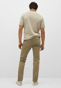 Chemise beige à manches courtes associée à un pantalon kaki, avec une coupe slim et des poches arrière. L'ensemble est complété par des baskets blanches.