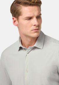 Camisa de botones gris claro con cuello puntiagudo, textura suave y dos botones en la tapeta, exhibida sobre un fondo neutro.