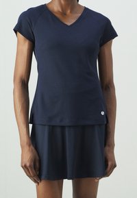 Granatowy sportowy top z krótkimi rękawami i dekoltem w serek, zestawiony z dopasowaną spódnicą, ozdobioną logo w pobliżu brzegu.