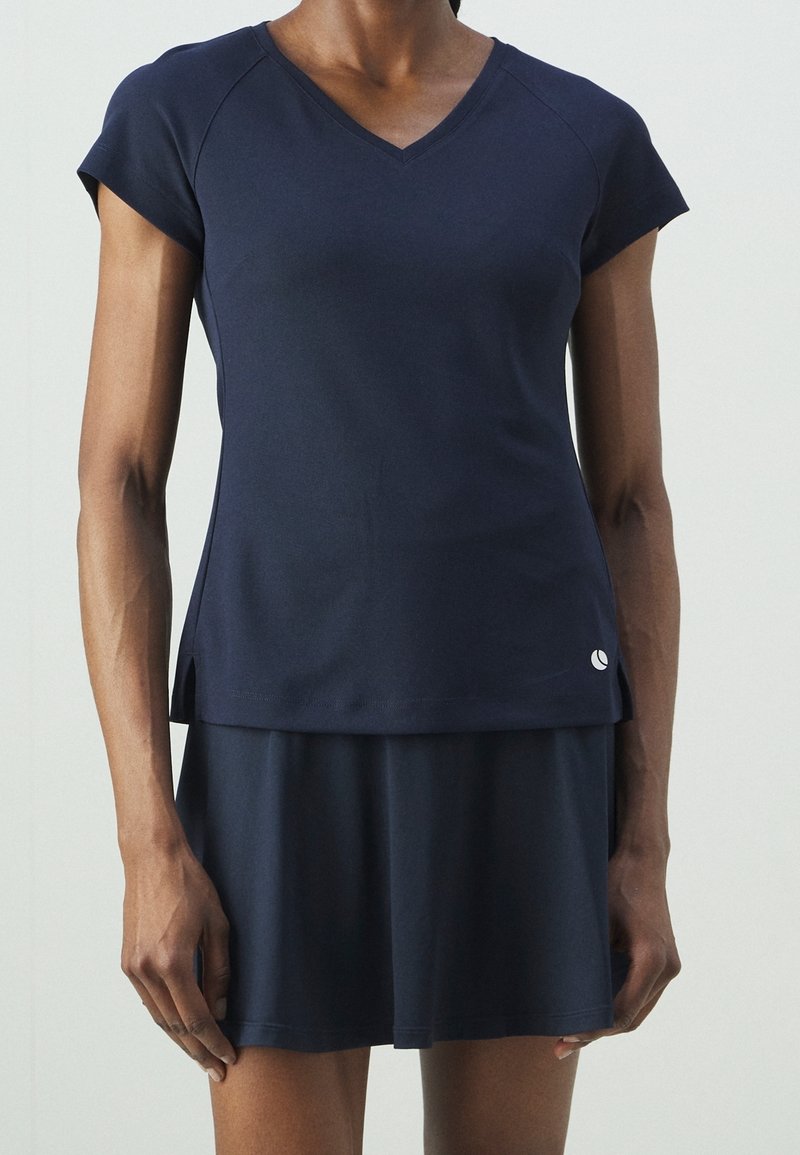 Granatowy sportowy top z krótkimi rękawami i dekoltem w serek, zestawiony z dopasowaną spódnicą, ozdobioną logo w pobliżu brzegu.