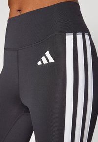 Legging sportivi neri con vita alta, caratterizzati da tre strisce verticali bianche sul lato e un logo bianco sulla coscia.