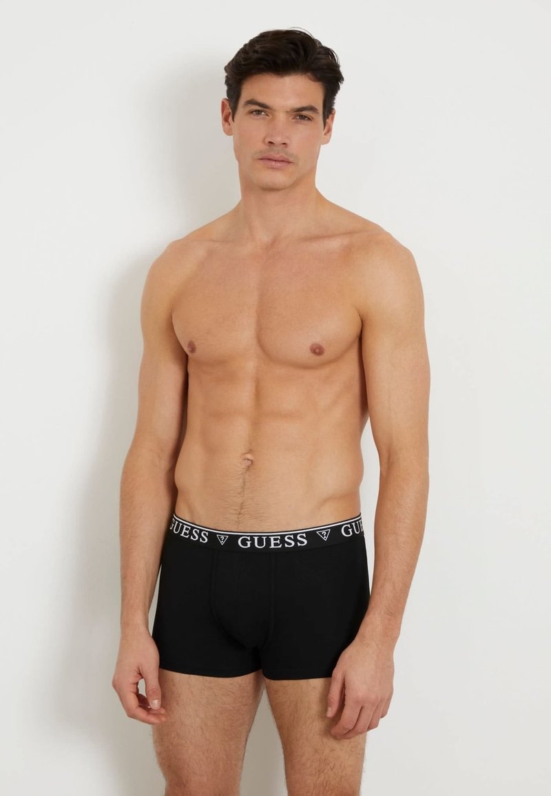 Fekete boxer alsónadrág fehér márkázott derékszíjjal, amelyen a "GUESS" felirat olvasható. Az anyag simának és illeszkedőnek tűnik. Nincsenek további minták.