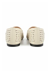 Zapatos beige sin cordones con patrones florales recortados, material de cuero, textura suave y una suela negra baja. Vista trasera que muestra el diseño.