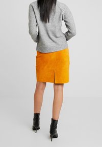 Gonna a matita in suede arancione con spacco posteriore, abbinata a un maglione in maglia grigio. Stivaletti neri con lacci completano l'outfit.