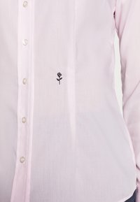 Camicia button-up rosa chiaro realizzata in misto cotone, con un piccolo motivo di rosa ricamato in nero sul lato sinistro e bottoni simili a perle.