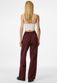 Pantalons larges bordeaux avec des rayures verticales, taille élastique et texture lisse, associés à un débardeur ajusté blanc.