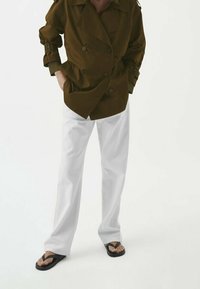 Brązowa dwurzędowa marynarka z dużymi klapami, połączona z białymi spodniami i czarnymi klapkami. Marynarka ma podszycie na ramionach oraz guziki.