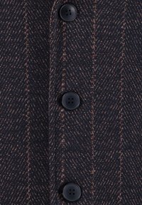 Niebieski materiał w wzór jodełki z pomarańczowymi akcentami, z czarnymi guzikami. Tekstura jest tkana, co zapewnia elegancki, ale jednocześnie wytrzymały wygląd.