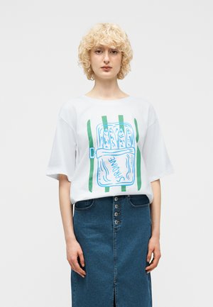 Lyshåret person iført en hvid t-shirt med en blå og grøn dåse sardiner-grafik og et højtaljet knaplukket denimnederdel.