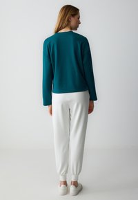 Felpa teal con spalle abbassate, maniche lunghe e orlo arrotondato, abbinata a joggers bianchi affusolati e sneaker bianche.