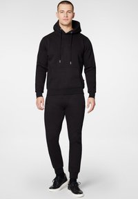 Czarny komplet z dresu składający się z bluzy z kapturem i spodni dresowych, wykonany z miękkiego materiału. Bluza posiada kieszeń z przodu i sznurki; spodnie mają boczne paski i ściągacze przy nogawkach.