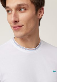 White cotton t-shirt with a multicolored striped collar and a small turquoise logo, featuring a smooth texture and a classic fit.