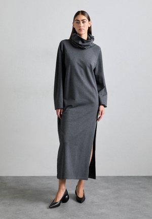 Gray jersey maxi dress with a high cowl neck, long sleeves, and side slit. Paired with black pointed-toe heels on a neutral background.