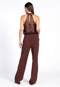 Bruine haltertop met knoopdetail bij de hals, gecombineerd met high-waisted, wijdvallende bruine broeken. Gladde textuur en op maat gemaakte pasvorm.