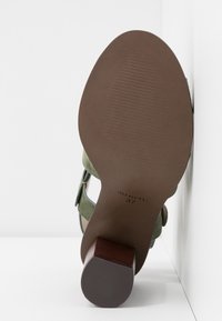 Semelle d'une chaussure à talon haut en daim vert avec un talon marron texturé et la taille 37 visible en dessous.