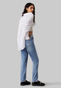 Camisa blanca de gran tamaño con mangas largas, combinada con jeans de tiro alto de color azul claro y zapatos negros, con un corte relajado y un diseño sencillo.