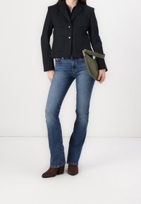 Granatowa, strukturalna marynarka z srebrnymi guzikami i dużymi przednimi kieszeniami, w połączeniu z niebieskimi rozszerzanymi dżinsami i brązowymi botkami na obcasie. Zielona torebka kopertówka.