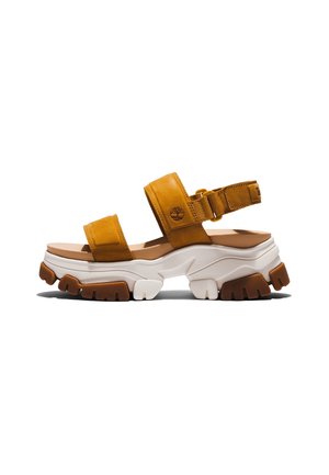Gruba sandałka z brązowymi skórzanymi paskami, regulowanym paskiem z tyłu, grubą białą i brązową solidną podeszwą oraz logo Timberland na bocznym pasku.