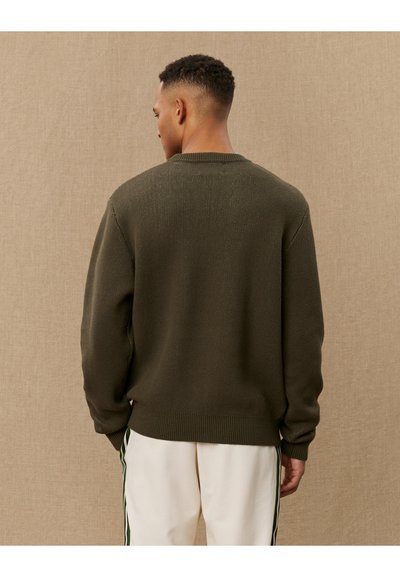 Pull en maille vert foncé avec un col rond et une bordure côtelée, présentant un motif texturé. Le dos est uni avec des manches montées.