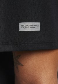 Tela atlética negra con una etiqueta rectangular blanca que dice "NIKE PERFORMANCE SPORT APPAREL"; textura suave, vista de cerca.