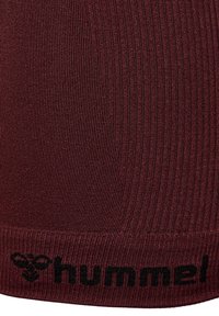 Primo piano di un tessuto rigato color maroon con il logo "hummel" nero e un'emblema stilizzato di un'ape sul bordo inferiore.