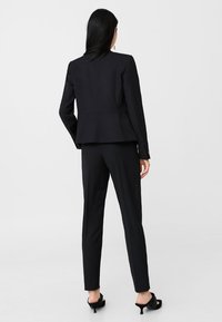 Costume noir comprenant un blazer ajusté et un pantalon slim, confectionné dans un tissu lisse. Design simple sans motifs ni embellissements visibles.