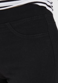 Černé džínové jeggings s hladkým povrchem, které mají zakřivenou přední kapsu a kontrastní stehy podél švů.