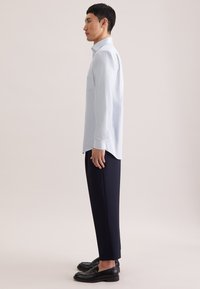 Hellblaues Hemd mit Knöpfen und geometrischem Muster, kombiniert mit dunkelblauen Hosen und schwarzen Loafers, seitlich dargestellt.