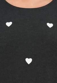 Μαύρο μπλουζάκι με τρία μικρά λευκά σχέδια καρδιών σε κατακόρυφη διάταξη στο μπροστινό μέρος. Το ύφασμα φαίνεται μαλακό και με υφή.