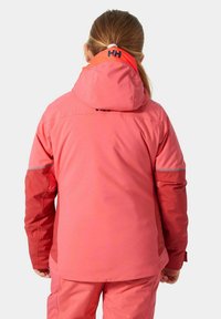 Giacca impermeabile rosa con cappuccio, caratterizzata da dettagli riflettenti e una texture liscia. La parte posteriore presenta un logo all'altezza del collo.