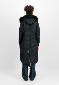Svart lang puffjakke med hette i kunstpels, med glidelås, sidelommer og en høy-lav kant med justerbare snorer.