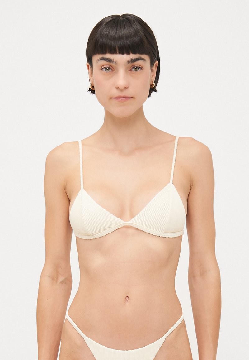 Crème-kleurige bikini-top met ribbelstructuur, driehoekige cups en dunne verstelbare bandjes. Eenvoudig ontwerp en minimalistische hardware-accenten.