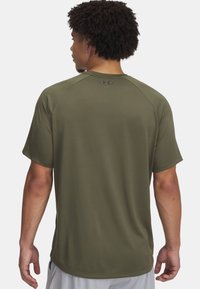 Camiseta atlética de manga corta color verde oliva con una textura suave, mangas raglán y un logo en la parte posterior cerca del escote.