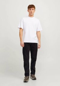 Biała bawełniana koszulka z krótkim rękawem, zestawiona z czarnymi spodniami i szarymi tenisówkami. Strój ma prosty, codzienny design.