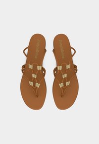 Καφέ επίπεδα σανδάλια με πολλαπλούς λεπτούς ιμάντες και χρυσά πλεγμένα διακοσμητικά στοιχεία, απεικονιζόμενα από πάνω σε απλό φωτεινό φόντο.