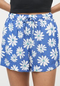 Μπλε σόρτς με λευκό σχέδιο από λουλούδια μαργαρίτας και ζωνάκι με κορδόνι που δένει, φορεμένα με μαύρο cropped τοπ.