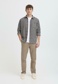 Camisa de cuadros en blanco y negro sobre una camiseta blanca, combinada con pantalones beige y zapatillas blancas, llevada por un modelo masculino.